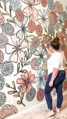 a woman standing in front of a wall with flowers painted on it and another person painting the wall behind her