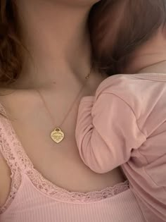 a woman wearing a pink shirt holding a small gold heart necklace on her chest and looking at the camera