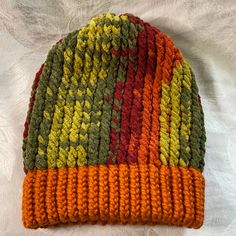 a multicolored knitted hat laying on top of a white sheet with an orange, green, yellow and red stripe