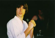 a man holding a microphone in his right hand and wearing a white shirt with rolled up sleeves