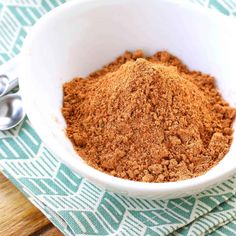 a white bowl filled with ground cinnamon on top of a green and white towel next to spoons