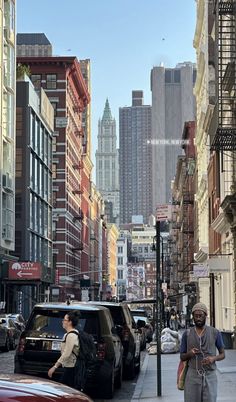 a man walking down the street in front of parked cars and tall buildings with skyscrapers behind him