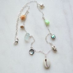 "This beautiful ocean inspired necklace features a sliced cowrie shell in the center with various shells, a white pearl and frosted glass dangling from a sterling silver 1.6mm long and short chain. Available in 18\" or 24\" lengths. Shells include pyrene, nassa, abalone, tapok, puka Also available in gold filled" Silver Necklaces With Charms For The Beach, Silver Necklace With Pearl Charm For Beach, Beach Jewelry: Silver With Pearl Charm, Beach Jewelry With Silver Pearl Charm, Silver Beach Jewelry With Pearl Charm, Silver Shell Jewelry With Pearl Charm, Beach Silver Jewelry With Pearl Charm, Silver Jewelry With Pearl Charm For Beach, Silver Mother Of Pearl Jewelry For Beach