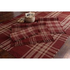 a red and white plaid rug with fringes on the floor next to a basket