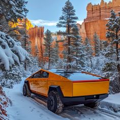 an orange car driving through the snow in front of some tall rocks and trees on a sunny day