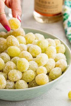 a woman is picking up some sugared donuts from a bowl on the table