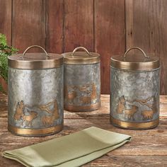 two metal canisters sitting on top of a wooden table next to a green napkin