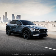 a gray mazda cx - 3 driving down the road in front of a city skyline