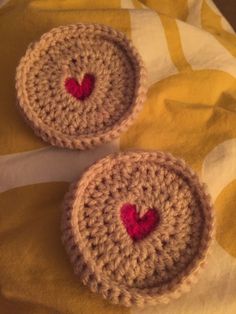 two crocheted bowls with red hearts on them sitting on a yellow and white blanket