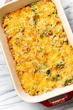 a casserole dish with broccoli and cheese in it on a marble surface