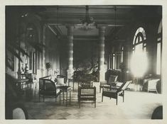 an old black and white photo of a living room with chairs, couches and lamps