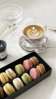 an assortment of macaroons in a black box next to a cup of coffee