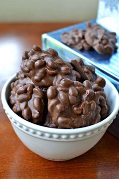 chocolate peanut clusters in a white bowl on a wooden table with text overlay that reads, peanuts clusters crockpot or microwave