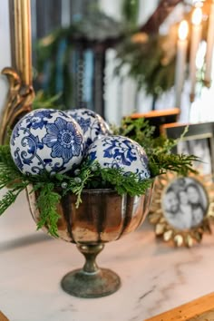 three blue and white ornaments are in a silver bowl on a marble table with greenery