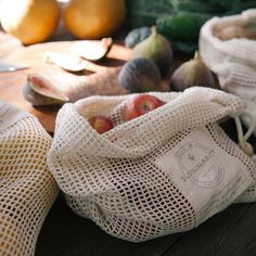 two bags filled with fruit sitting on top of a wooden table next to other fruits and vegetables