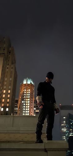 a man standing on steps in front of tall buildings at night with the city lights behind him