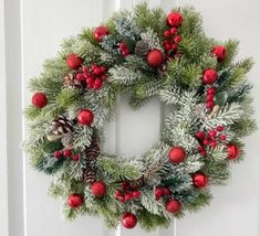 a christmas wreath hanging on the front door with pine cones and red balls around it