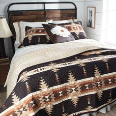 a bed with a brown and white quilt on it's headboard next to a night stand