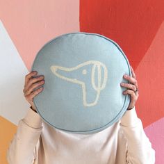 a woman holding up a pillow with a dog on it's face in front of a colorful wall