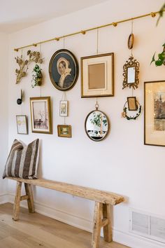 a wooden bench sitting in front of a wall covered with pictures and framed art on it