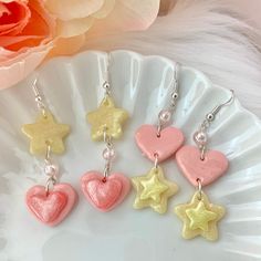 "These clay heart and star dangle earrings are handmade from polymer clay and add a kawaii touch to any outfit. The stars even glow in the dark! Made from special iridescent clay that shimmers in the light and embellished with an iridescent pink bead. - Dimensions: 1.5\" tall (2.5\" with earring hooks) - Silver-plated surgical steel hypo-allergenic earring hooks - Heart and star is coated in UV resin for protection and shine Available in two designs - heart or star dangle." Polymer Clay Star Earrings, Cute Earrings With Dangling Charms For Gifts, Cute Star Charm Dangle Earrings, Cute Dangle Earrings With Star Charm, Sweet Pink Dangle Heart Earrings, Sweet Pink Heart Dangle Earrings, Whimsical Heart Earrings For Gifts, Cute Dangle Jewelry With Star Charm, Pink Heart Charm Earrings