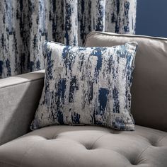 a couch with a blue and white pillow sitting on it's backrest next to a window