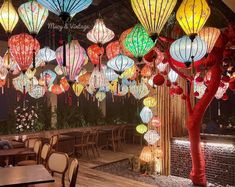 many colorful lanterns hanging from the ceiling above tables and chairs in a room with wood flooring