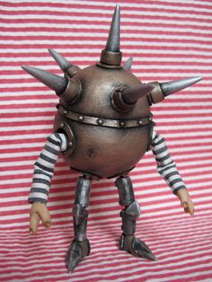 a toy robot with horns and spikes on it's head sitting on a striped cloth