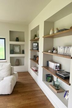 a living room filled with lots of white furniture and bookshelves next to a window