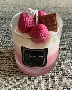 three strawberries in a small glass container with chocolate on the top and pink liquid