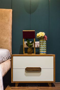 a nightstand with flowers on it next to a chair and bed in a room that has green walls