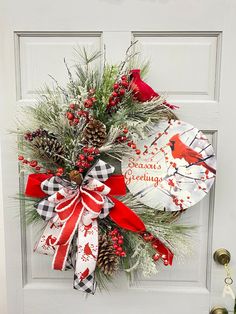 a christmas wreath on the front door with red and white ribbons, pine cones, evergreens and cardinals