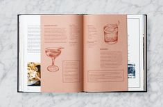 an open book with pictures of cocktails and drinks on the pages, sitting on a marble surface