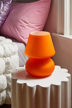 an orange lamp sitting on top of a white table next to a pile of pillows