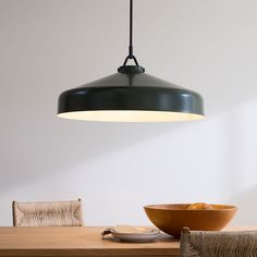 a black light hanging over a wooden table with a bowl on it and a chair in the background