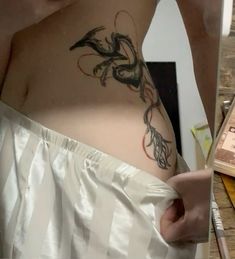 a woman with a dragon tattoo on her stomach and behind her is a white sheet