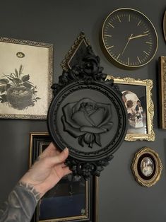 a person holding up a clock in front of some pictures and clocks on the wall