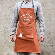 a man wearing an orange apron standing in front of a wall