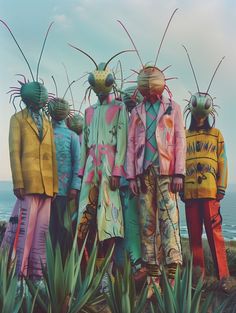 four people dressed in colorful clothing standing next to each other near the ocean with grasshoppers on their heads