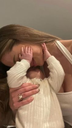 a woman holding a baby in her arms and kissing it's face with both hands