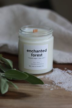 an enchanted forest candle sitting on top of a wooden table next to sea salt