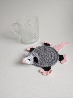 a small crocheted animal sitting next to a cup on a white table top