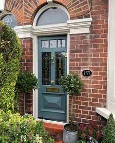 a green door with two potted plants next to it on the side of a brick building