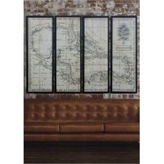 three framed maps on a brick wall above a leather couch