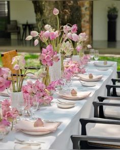 the table is set with pink and white flowers in vases, plates and glasses