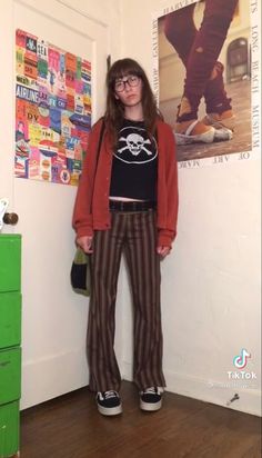 a woman standing in front of a wall with posters on it and wearing striped pants