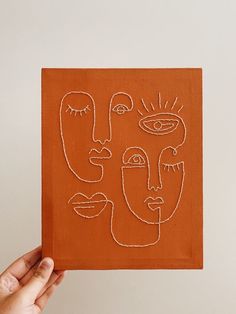 a hand holding up an orange piece of paper with faces drawn on it