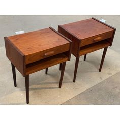 two small wooden tables sitting next to each other on top of a cement floor covered ground