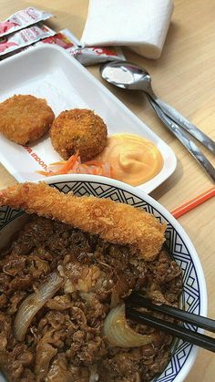 a bowl filled with meat and vegetables on top of a table next to utensils