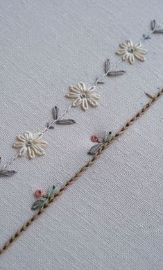 some white flowers and leaves are on a piece of fabric with thread in the middle